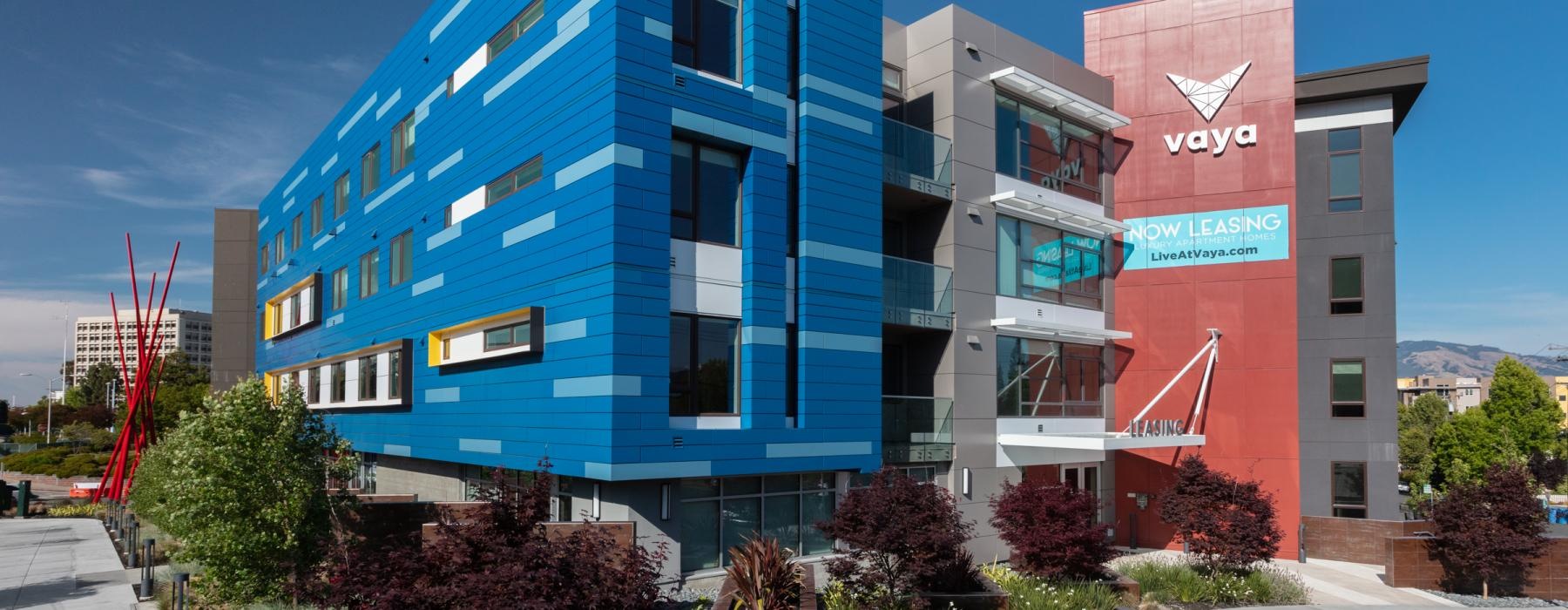 Exterior view of the brightly painted building in vibrant blue, red and gray hues at Vaya East Bay apartments for rent